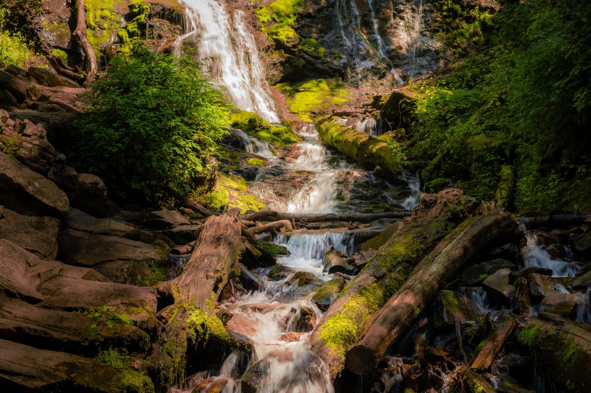 A wider view of Mingo Falls — more water and rock with forest floor in the foreground, seen from further down the trail.